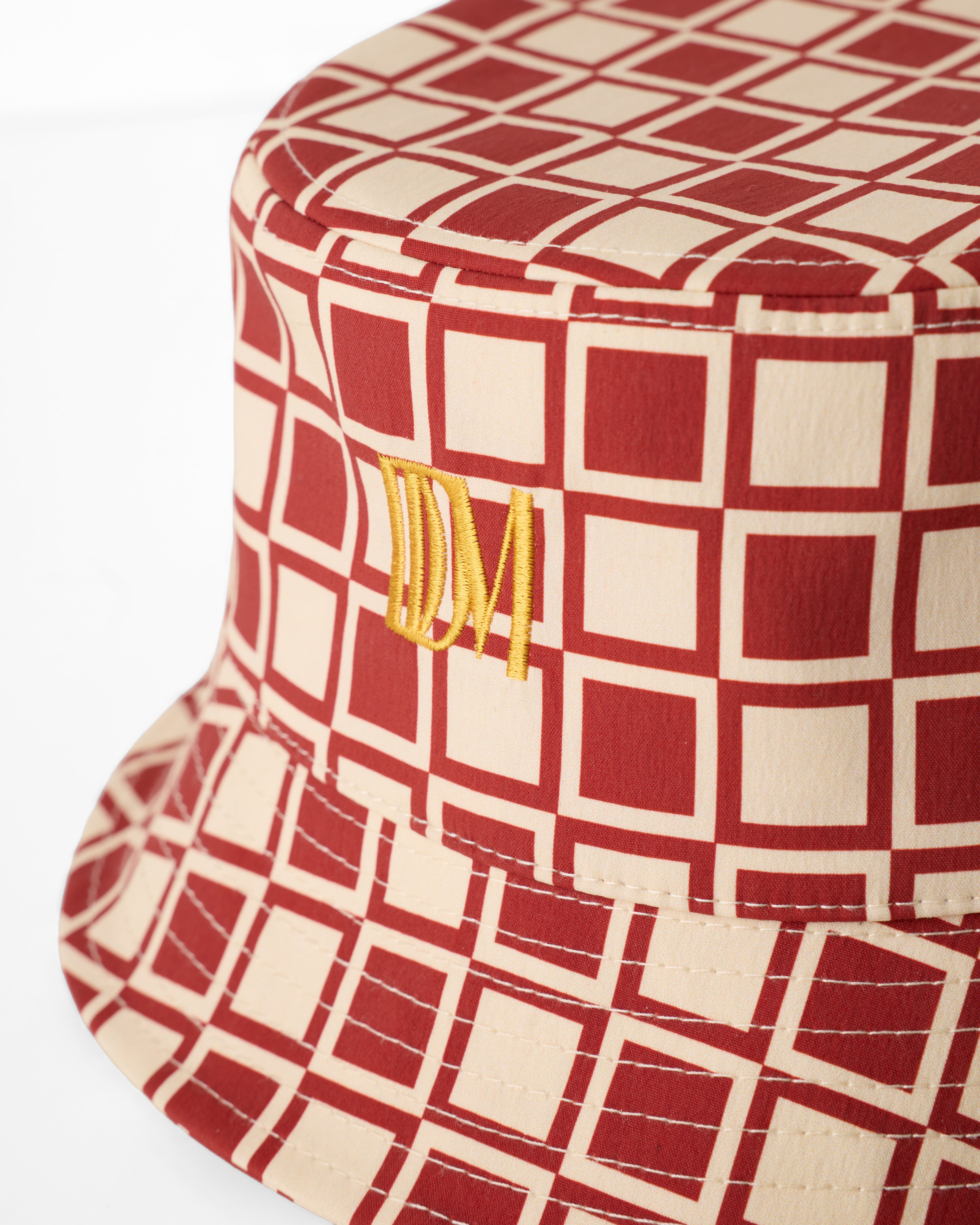 The Bucket Hat - Rouge by Dandy Del Mar features a red and beige geometric square pattern with yellow embroidered "IDM" initials on the front.