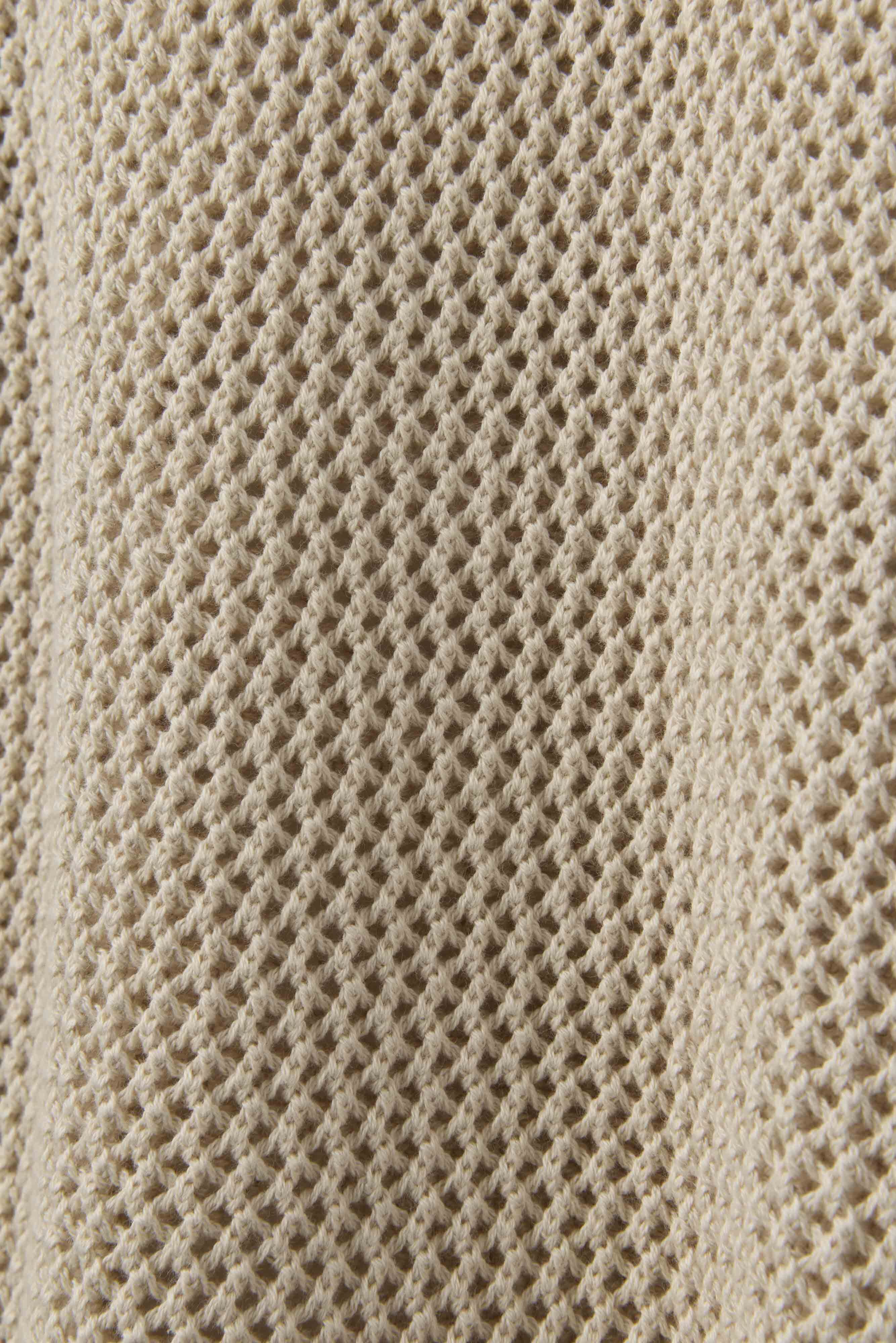 Close-up of The Porto Crochet Tank in Sabbia by Dandy Del Mar, highlighting its beige, textured, waffle-knit fabric with a grid-like open-knit pattern.