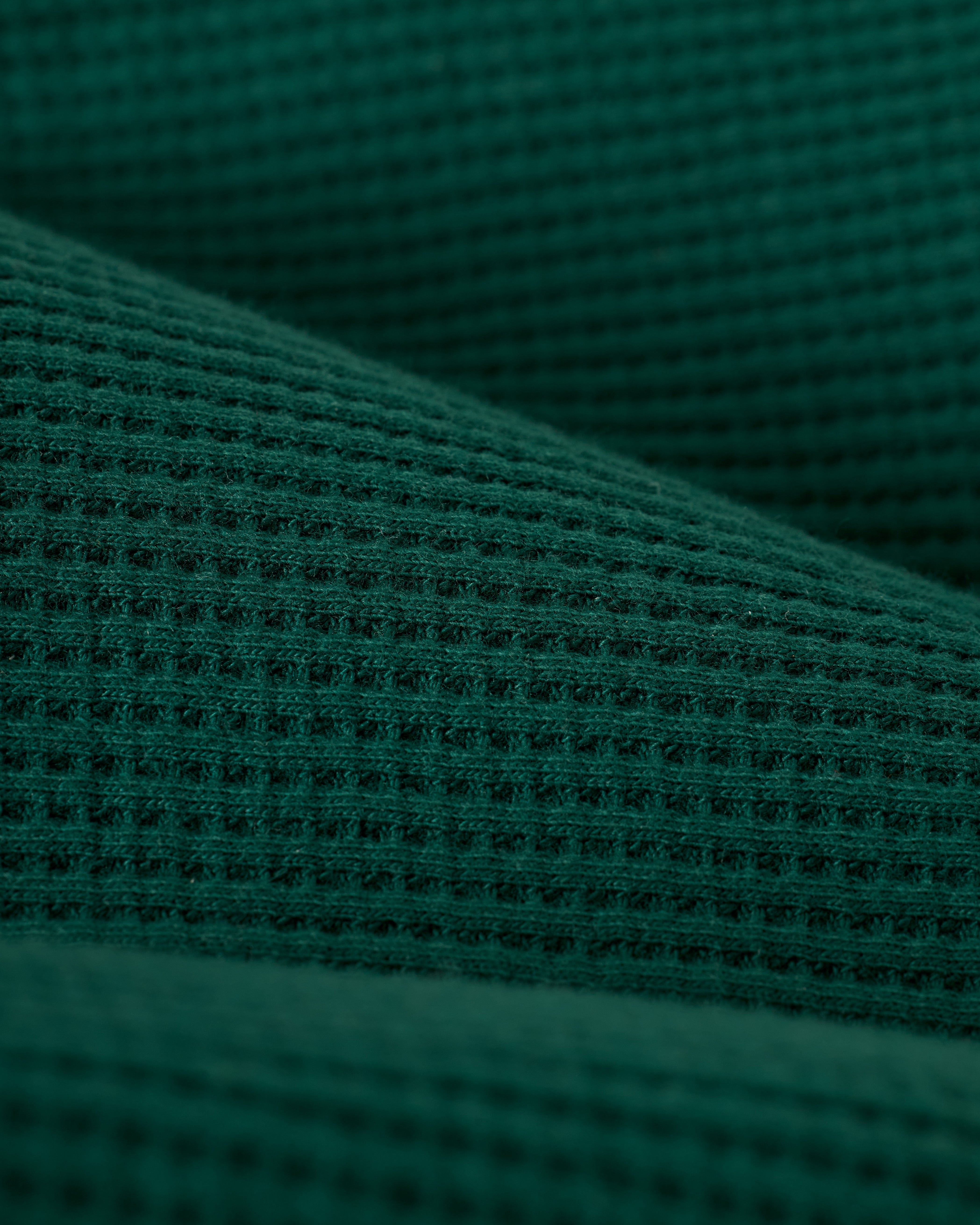 A detailed close-up of The Cannes Waffle Knit Shorts in Albero from Dandy Del Mar showcases the intricate dark green, waffle-textured fabric and its weave pattern.