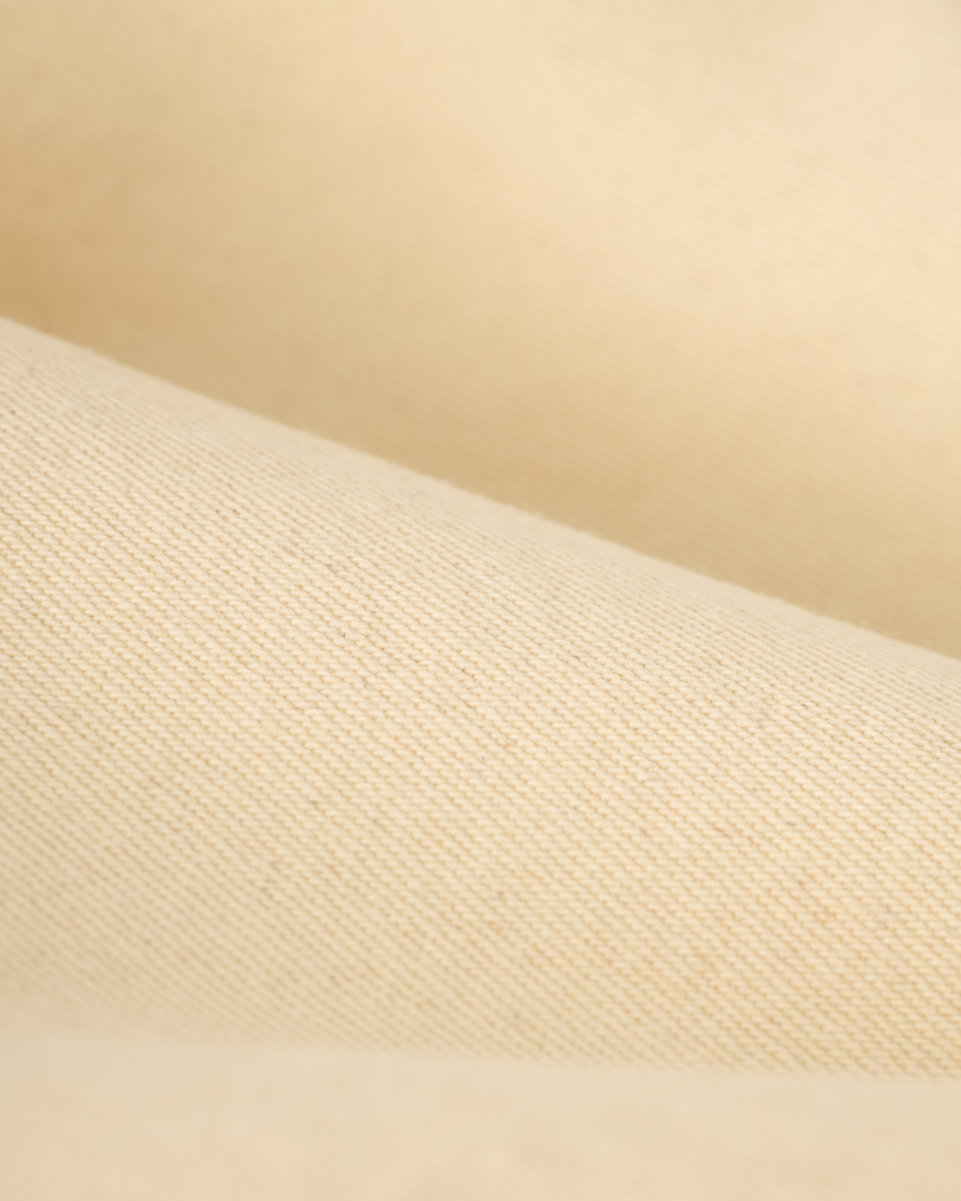 Close-up of folded denim shirt in beige with a smooth texture from The Cartagena Denim Shirt - Scallop collection by Dandy Del Mar.