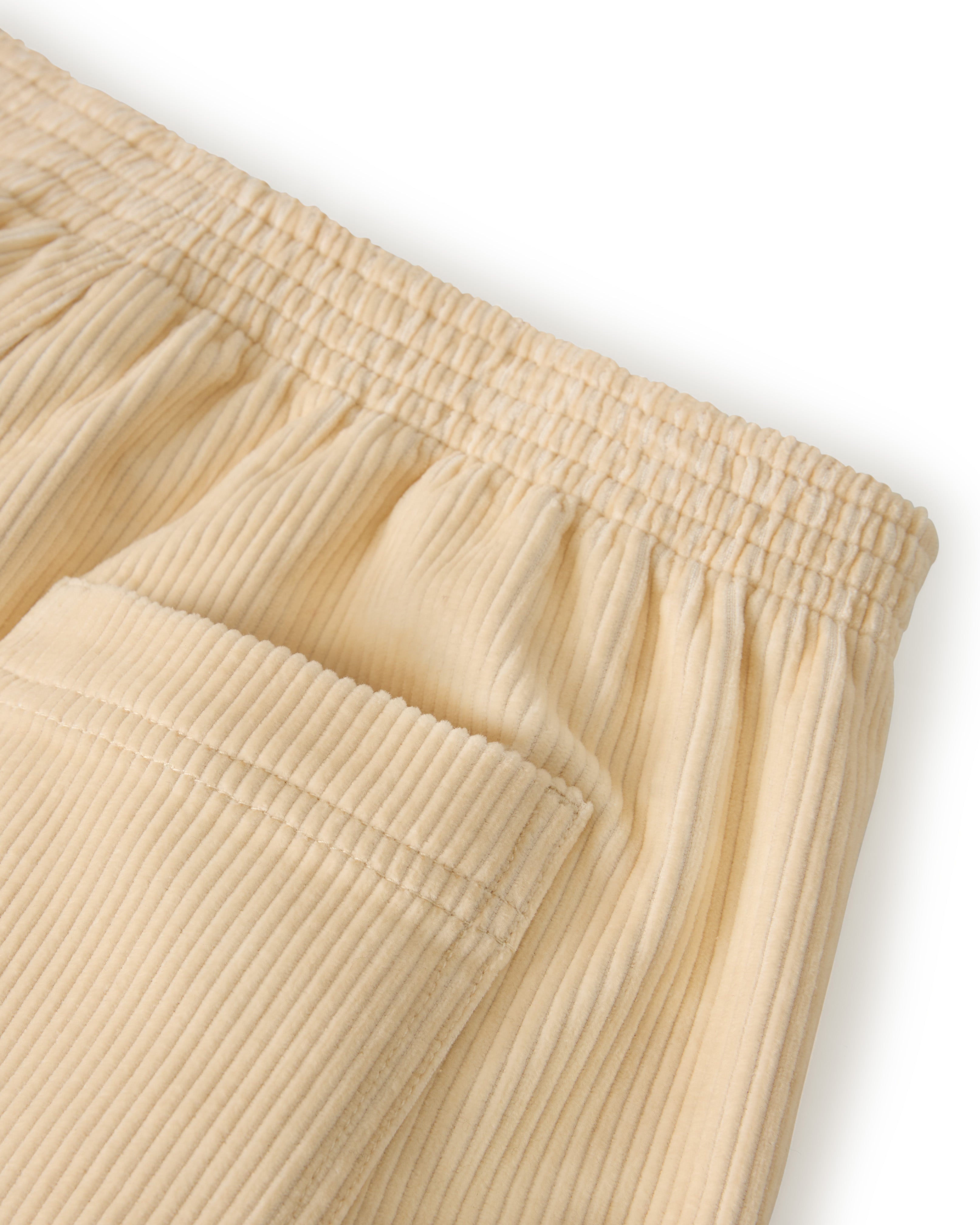 Close-up of The Corsica Corduroy Short - Scallop by Dandy Del Mar, featuring beige, ribbed fabric with an elastic waistband and a back pocket.