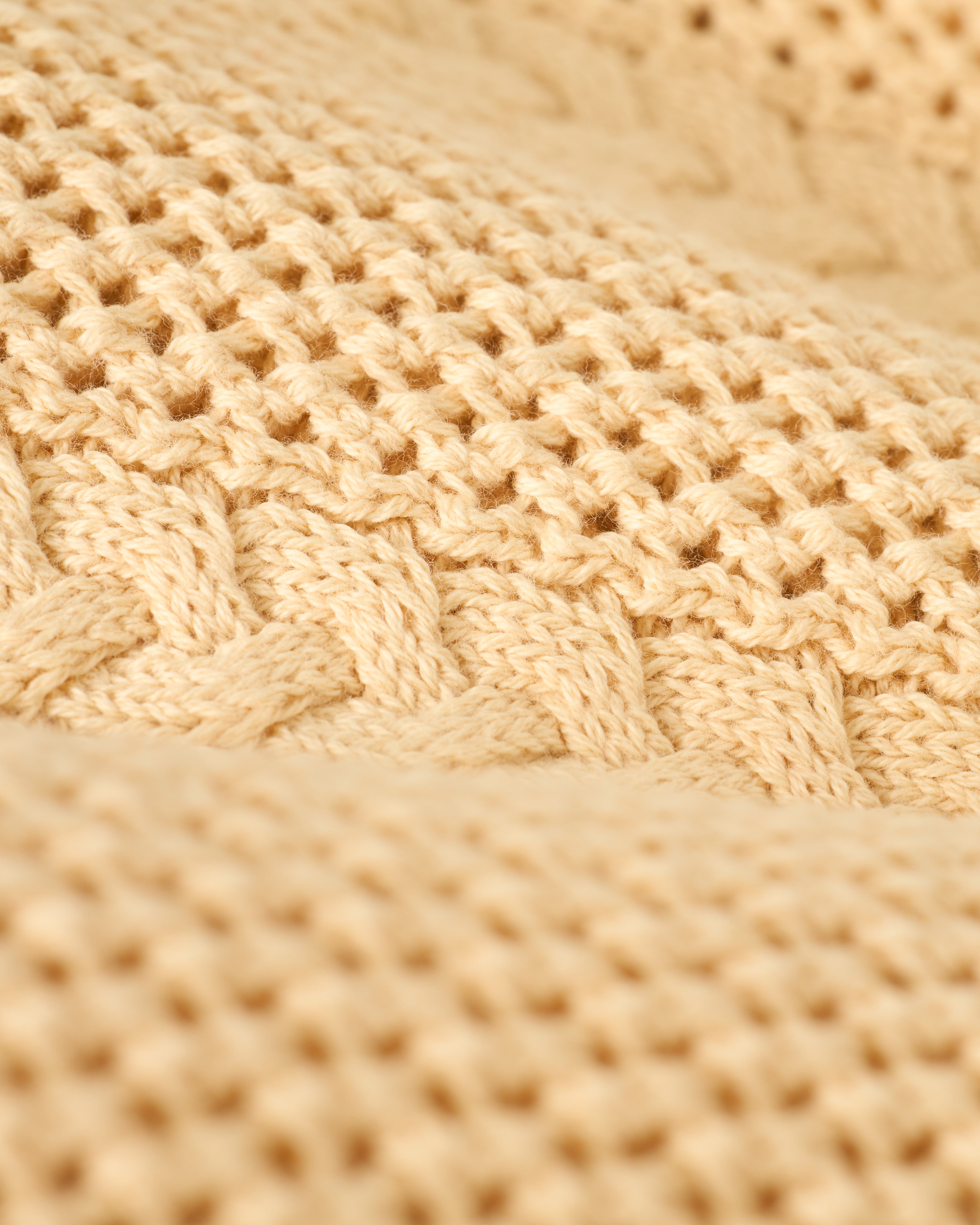 A close-up of The Crete Crochet Cardigan - Sabbia by Dandy Del Mar showcases its beige textured pattern of interwoven stitches.