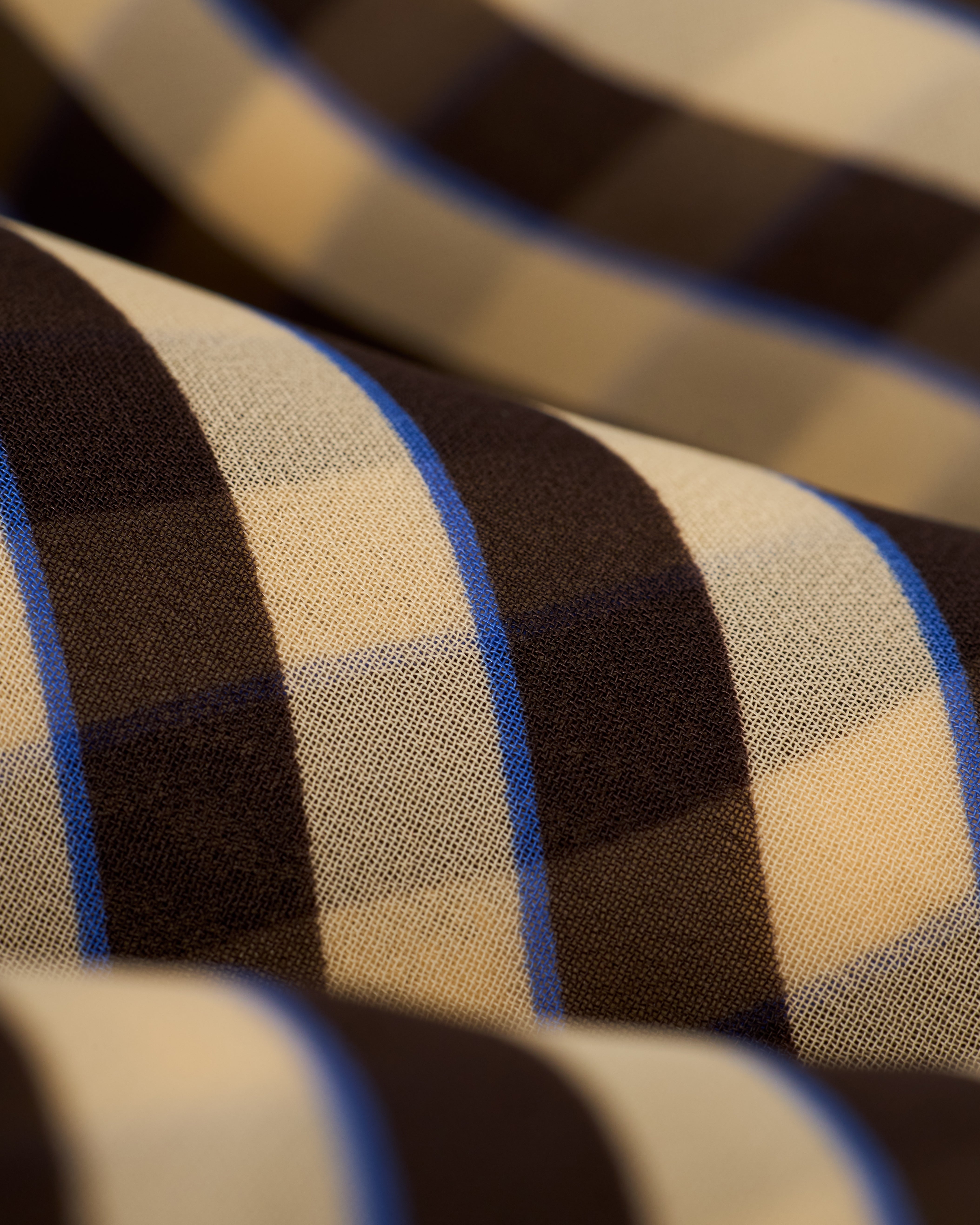 Close-up of Dandy Del Mar's The Curacao Short in Tierra, featuring a brown, cream, and blue plaid fabric with a diagonal orientation.