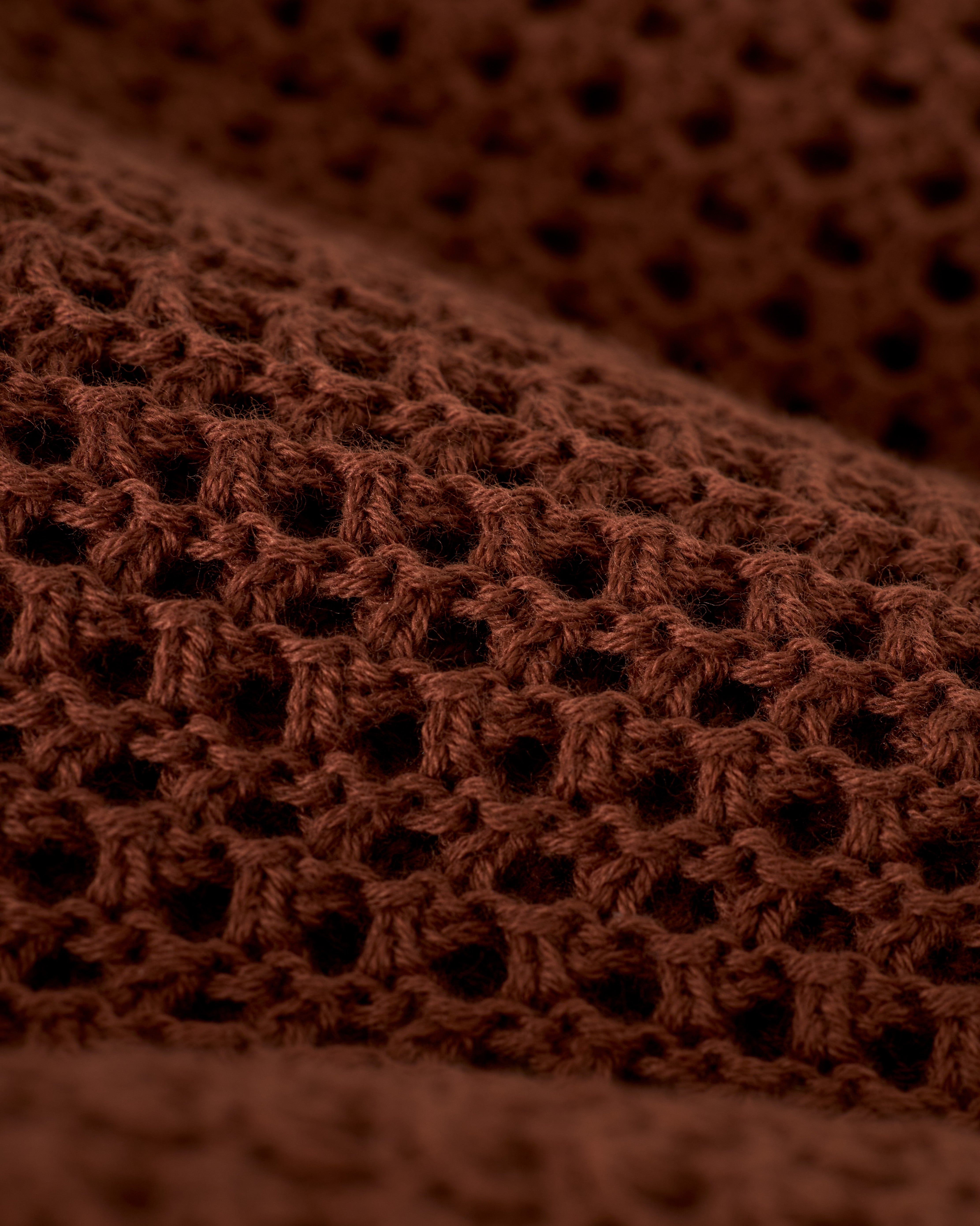Close-up of The Dominica Crochet Tank in Cappuccino by Dandy Del Mar, showcasing its lightweight brown knitted fabric and textured open weave design reminiscent of a relaxed-fit crochet top.