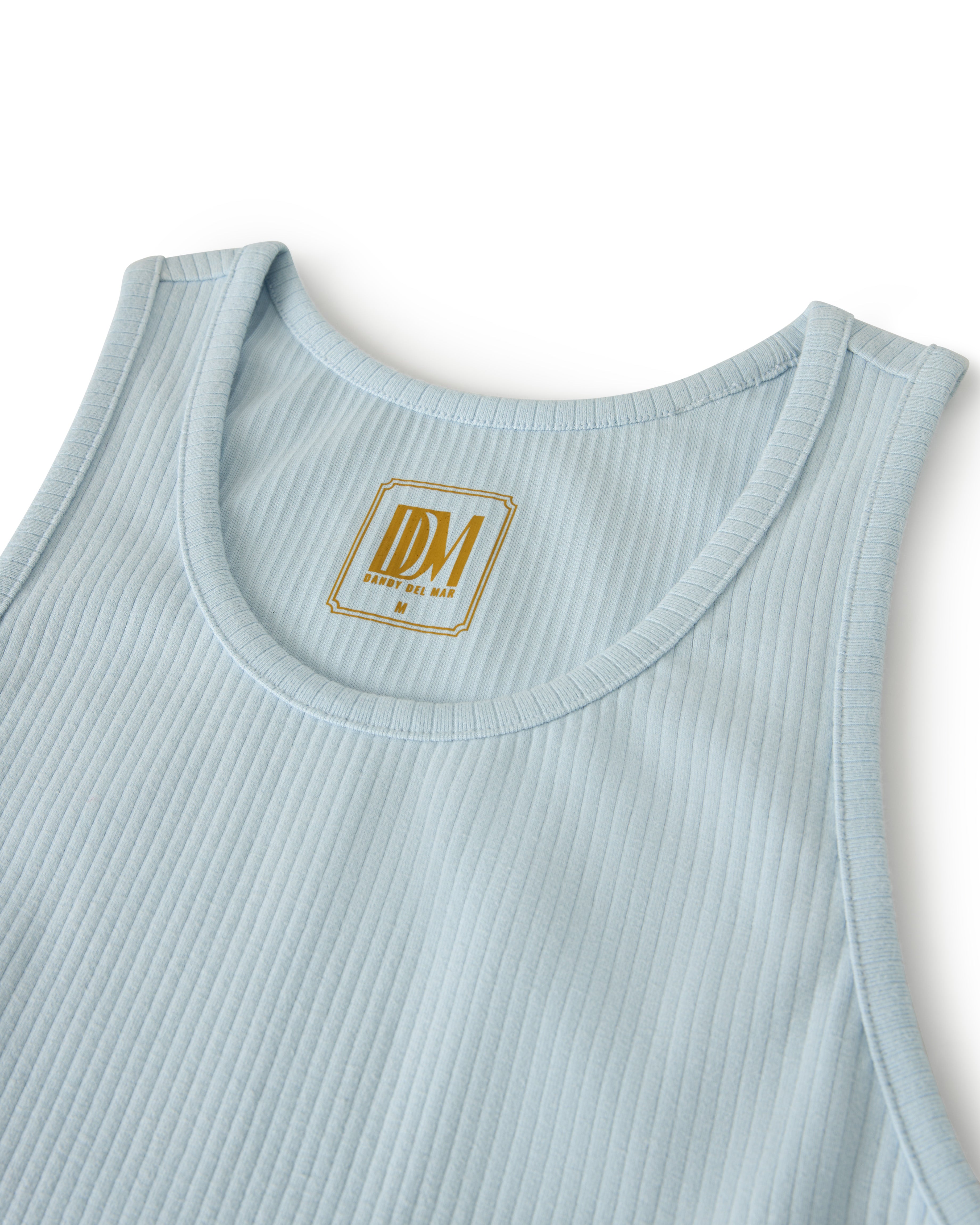 The Milan Rib Tank - Comet by Dandy Del Mar is a scoop neck light blue ribbed tank with stitched neckline and armholes, featuring a gold and white 'IDM Proudly Rich New' label inside, embodying luxury in simplicity.