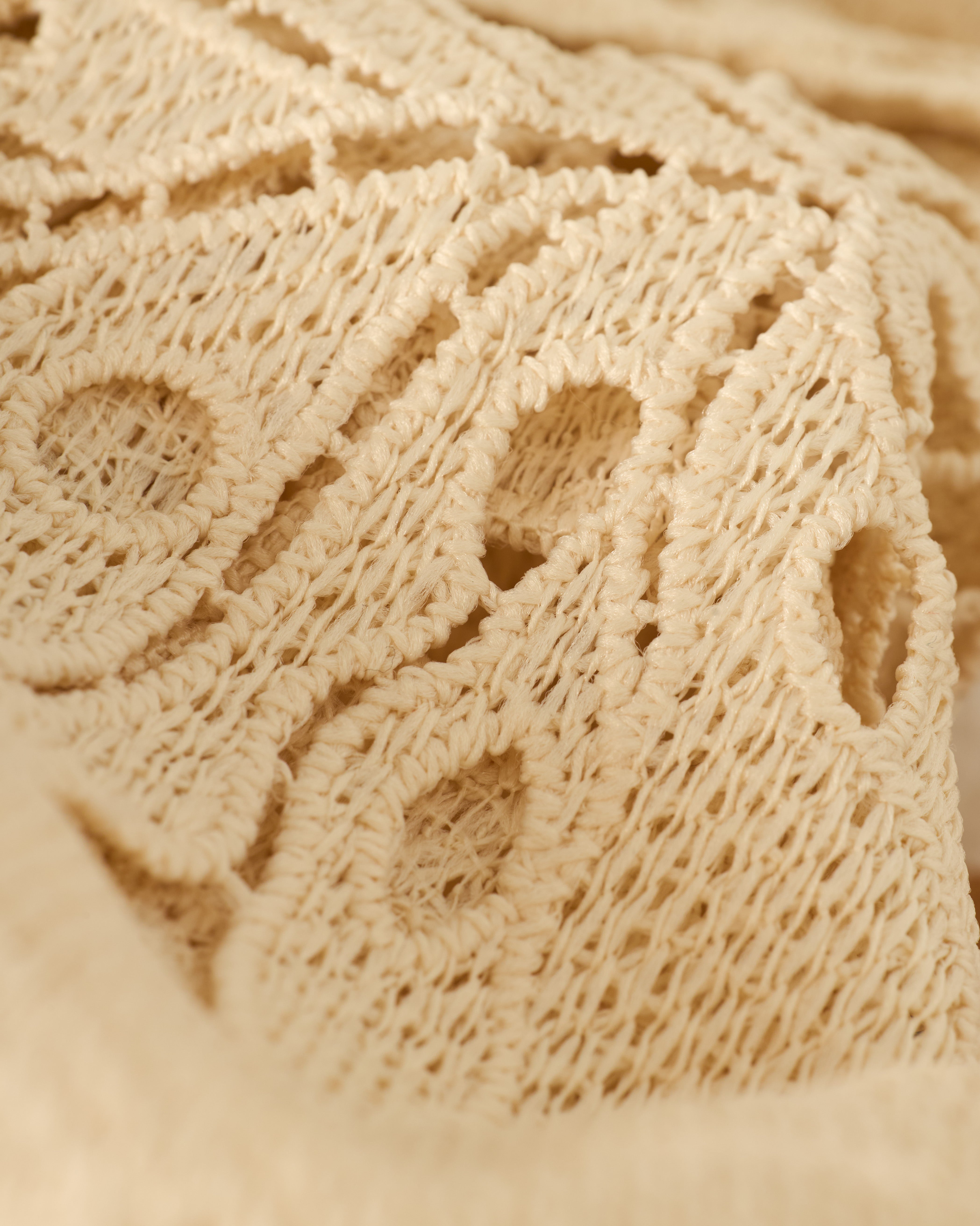 Detail of The Mara Tie Strap Dress - Scallop by Dandy Del Mar, showcasing beige knit fabric with an intricate lace-like pattern, featuring circular and linear designs.