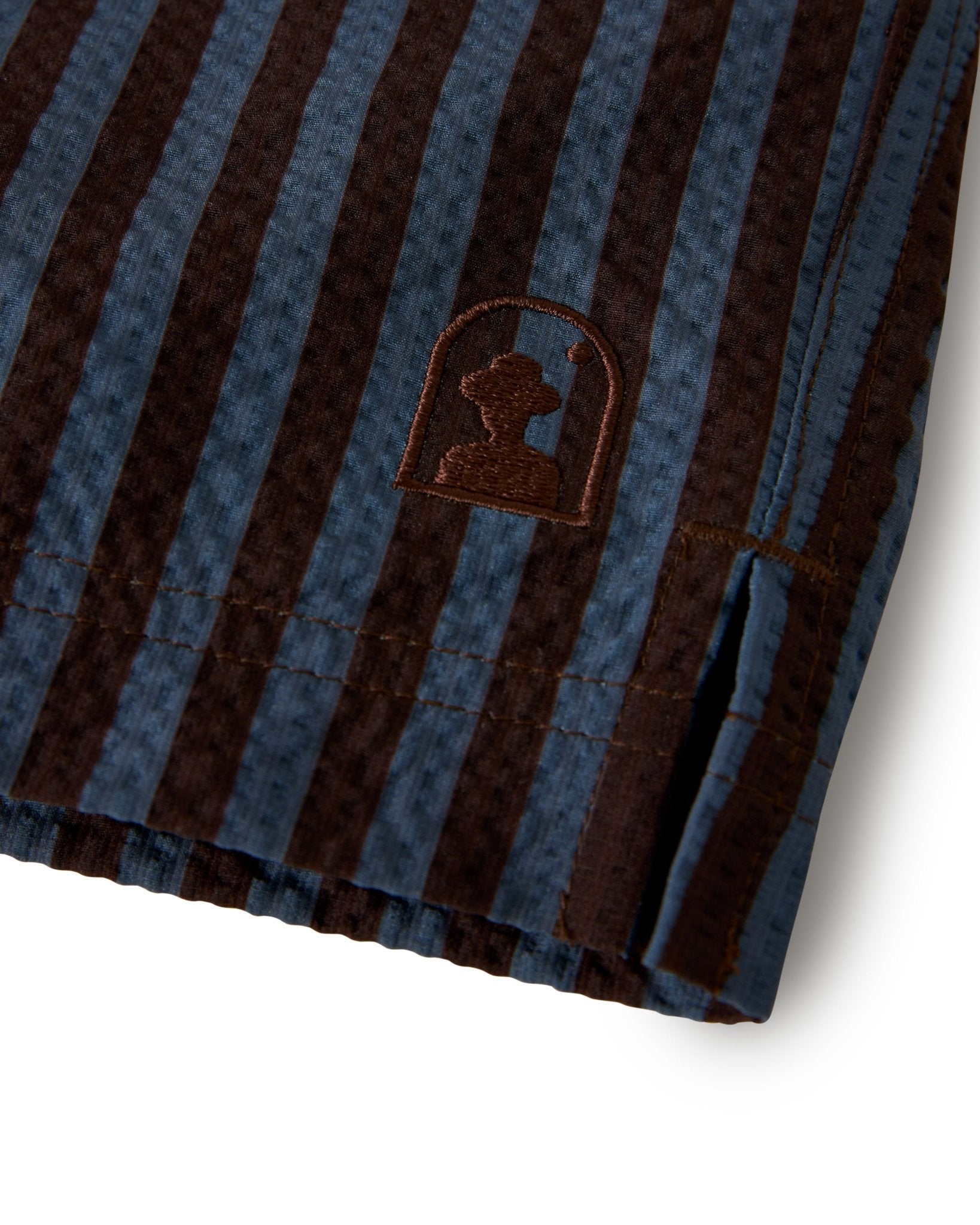 Close-up of The Ventura Volley Shorts - Moontide by Dandy Del Mar, showing blue and brown vertical stripes, an embroidered silhouette logo inside a rounded arch, and a comfortable elastic waistband.