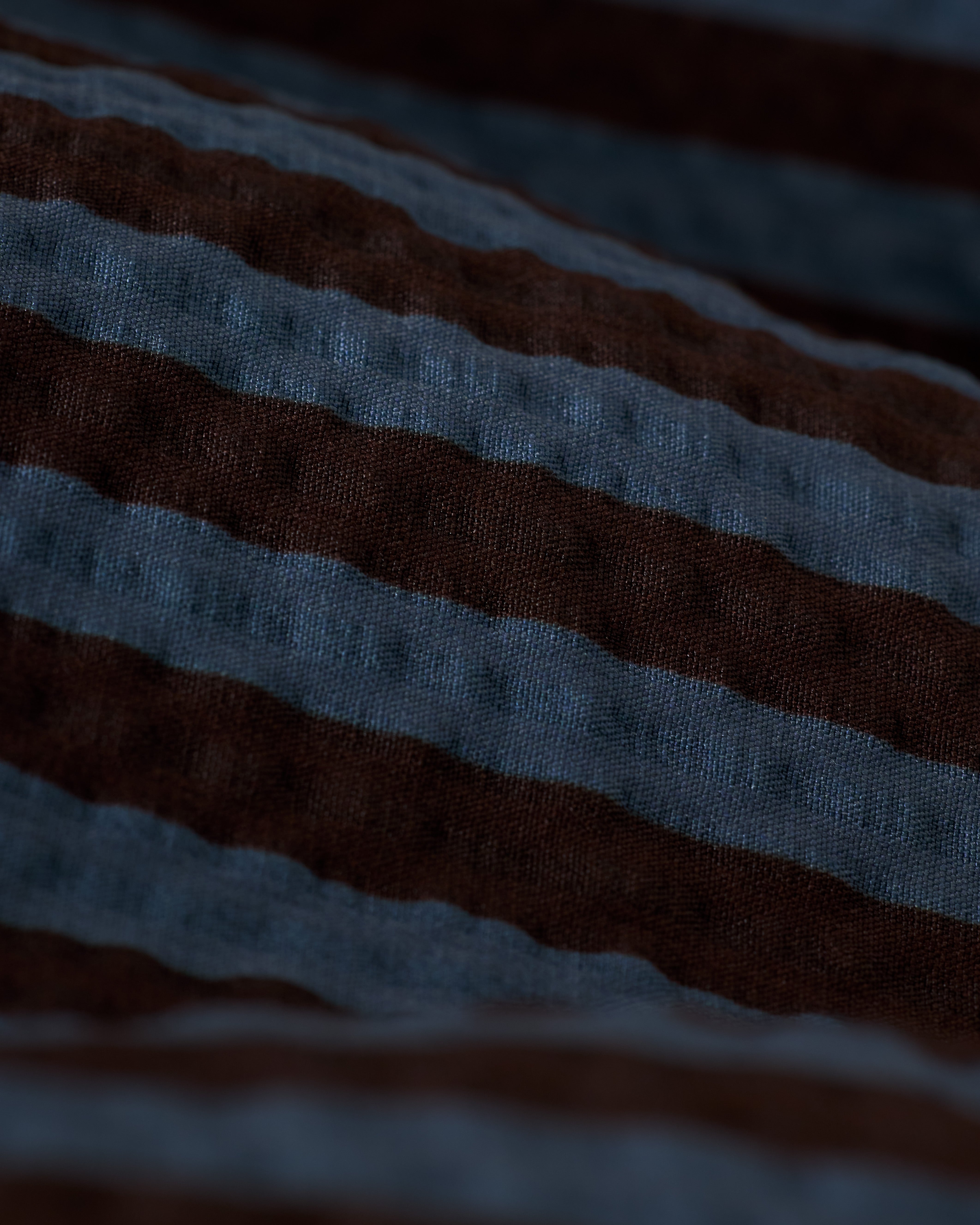 Close-up of The Ventura Volley Short - Moontide by Dandy Del Mar, featuring a dark brown and blue horizontal stripe pattern. Its micro mesh liner texture is slightly ribbed, resembling cozy swim shorts with an elastic waist.