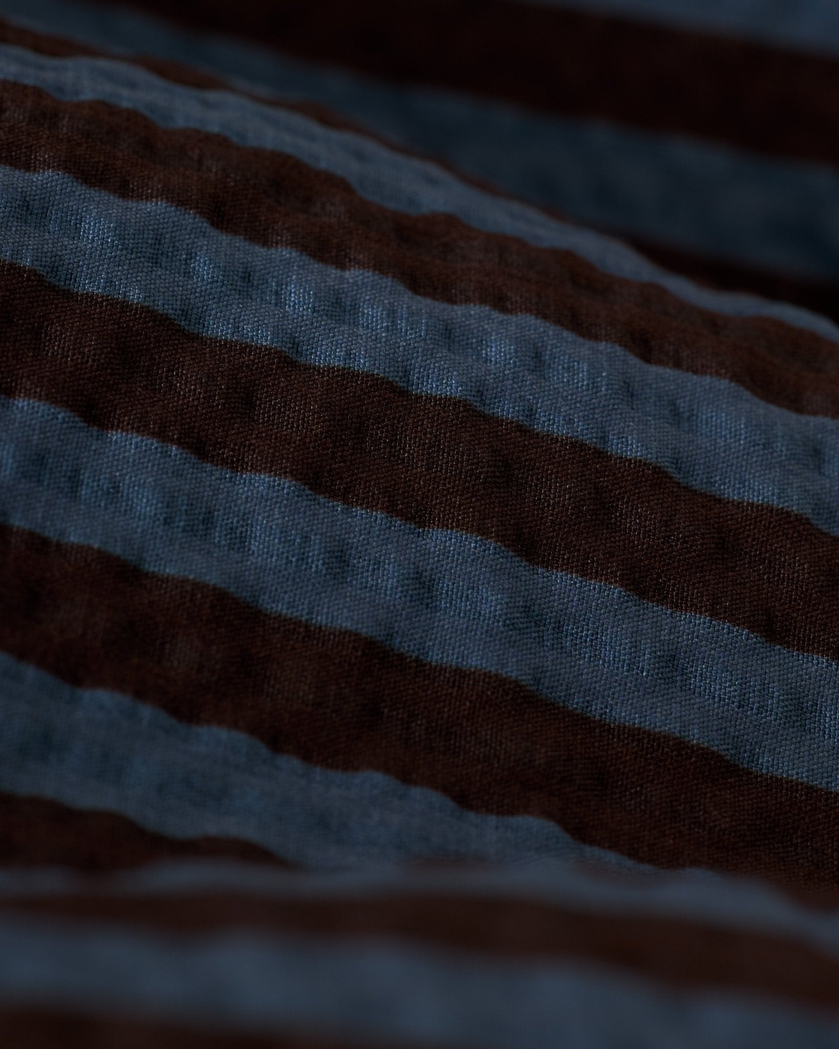 Close-up of The Ventura Volley Shorts - Moontide by Dandy Del Mar, showcasing the textured fabric with horizontal dark brown and blue stripes, visible folds, and elastic waist detail.