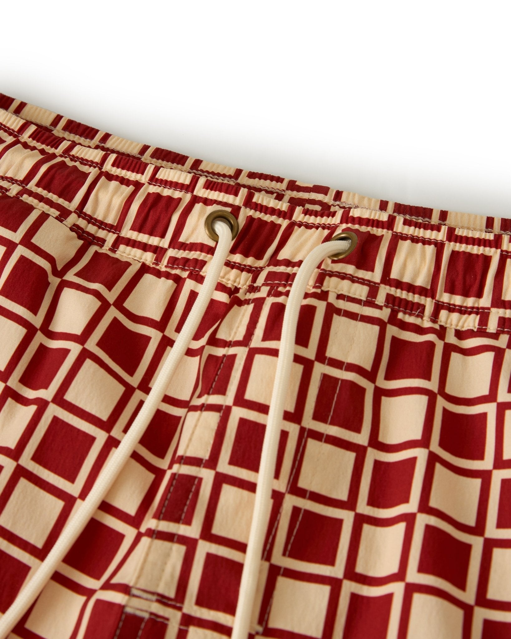 Close-up of The Ventura Volley Shorts - Rouge by Dandy Del Mar, featuring a red and beige geometric pattern, elastic waist, and white drawstrings.