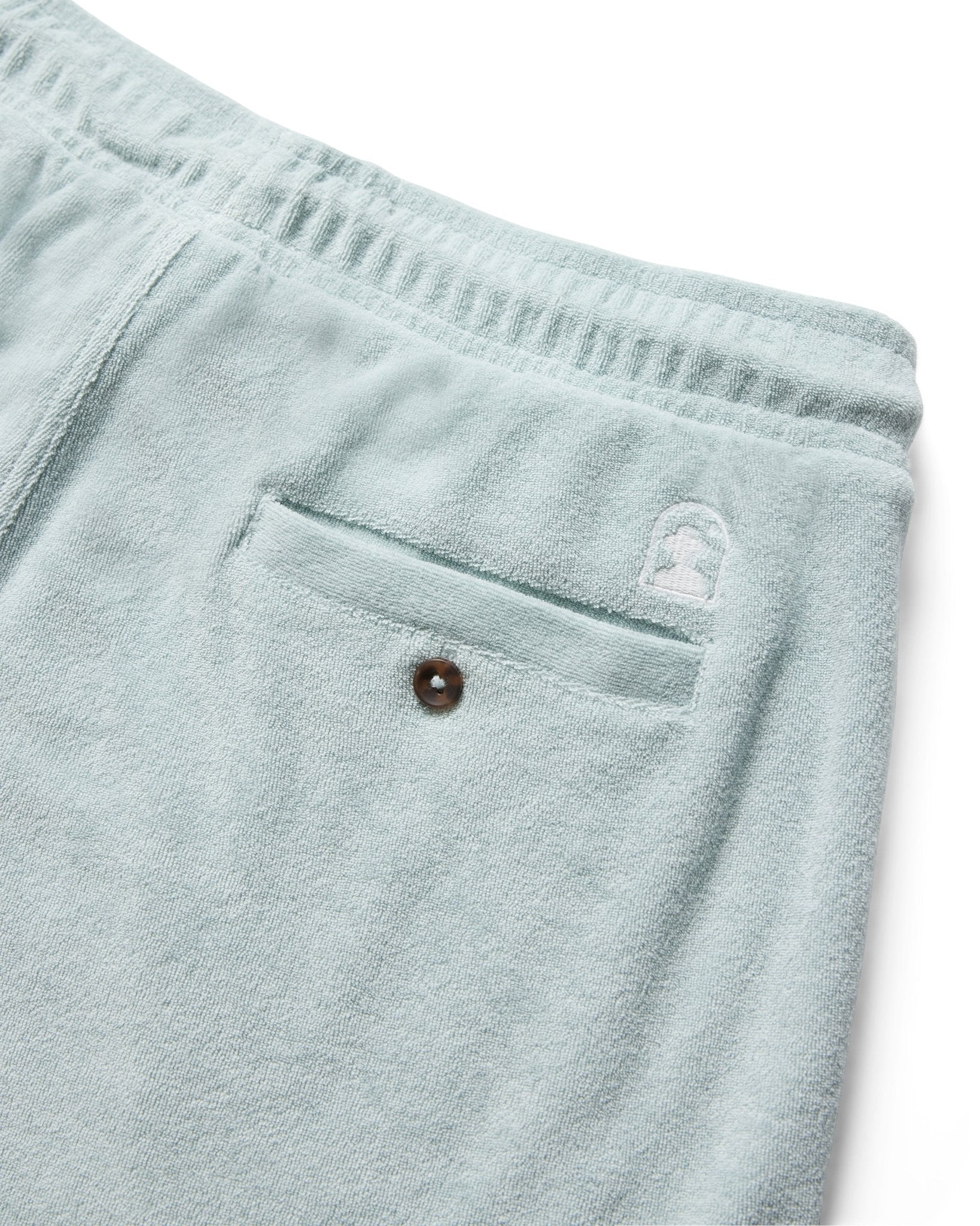 Close-up of the back pocket on Dandy Del Mar’s Tropez Terry Cloth Shorts in Gulf Blue, featuring an elastic waistband, a buttoned pocket, and a small embroidered logo above the pocket.