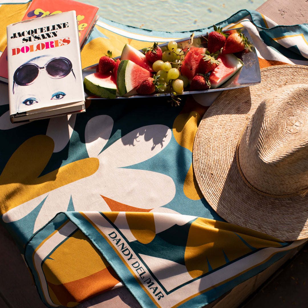 A towel with fruit and a book on it next to a pool.
