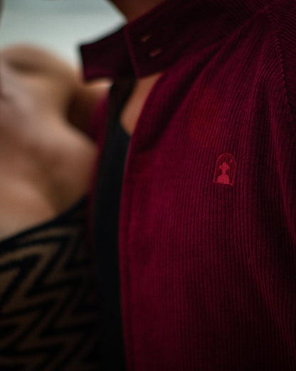 Close-up of two people, one wearing The Corsica Corduroy Jacket - Sangria from Dandy Del Mar, and the other with a patterned Gardenia jacquard silk top.