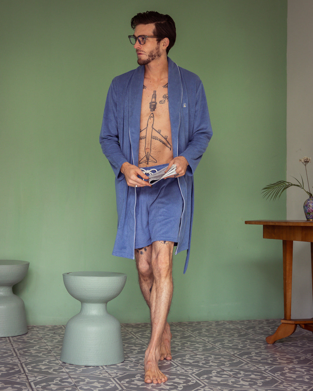 Man in a blue Dandy Del Mar Tropez Robe - Annapolis holding glasses, standing in a room with a green wall and patterned floor.