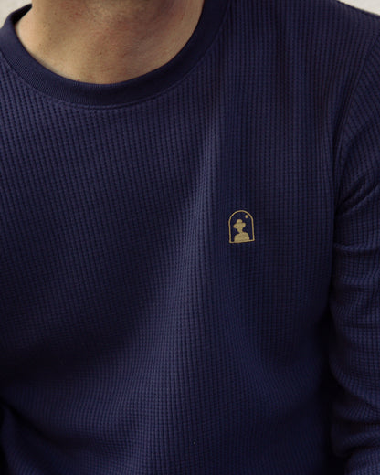 Close-up of a person wearing The Cannes Long Sleeve Shirt - Luxe Navy by Dandy Del Mar, adorned with a small gold chess knight emblem on the chest.