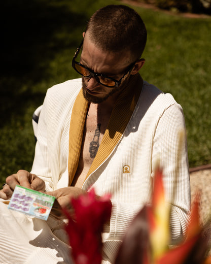 A man in a white suit holding a Dandy Del Mar Cannes Waffle Knit Robe - Vintage Ivory card.