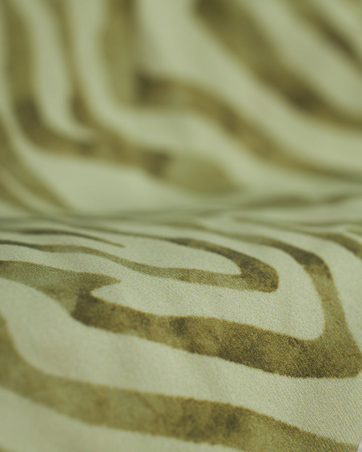 Close-up image of The Avila Top - Arbequina by Dandy Del Mar, featuring a light green and dark green abstract wavy pattern crafted from recycled nylon.