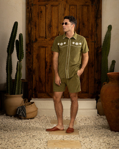 A man in a green Gaucho Short - Arbequina by Dandy Del Mar and shorts standing in front of a cactus.