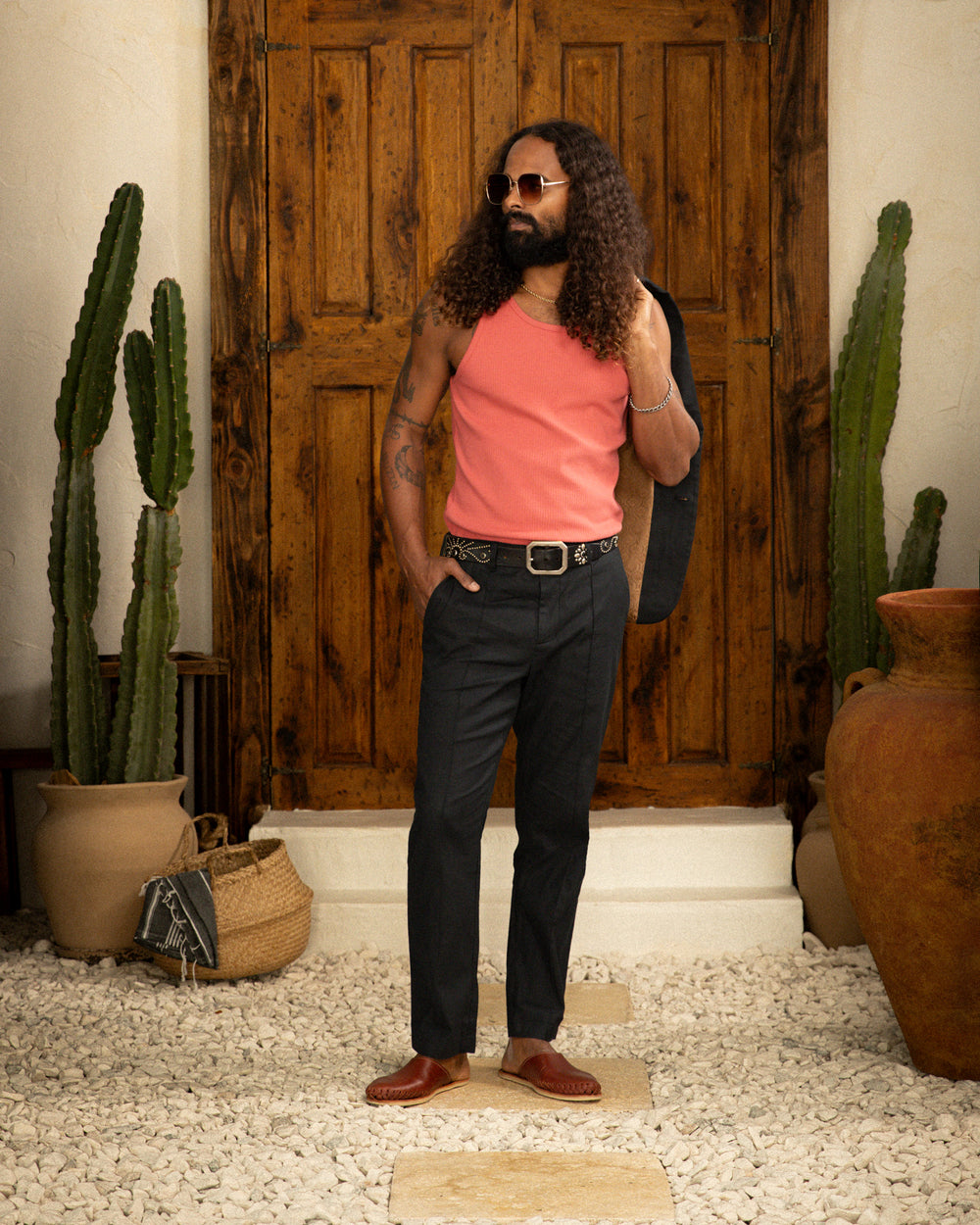 A man in a pink tank top standing in front of a wooden door, wearing a Dandy Del Mar Brisa Linen Trouser - Onyx.
