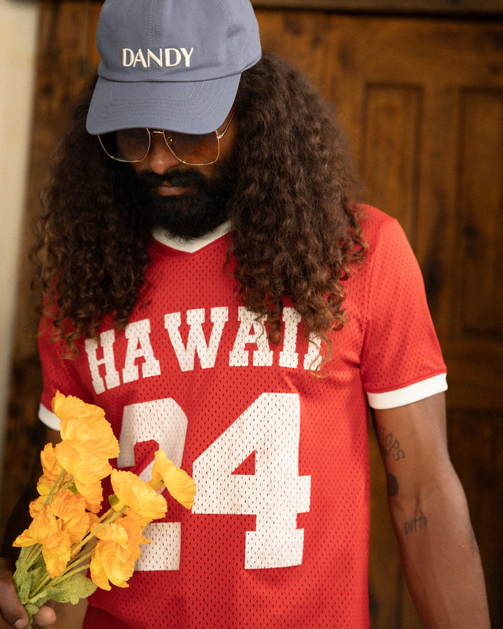 A man with long hair and a beard wearing a Hawaiian Kaena Mesh Tee from Dandy Del Mar.