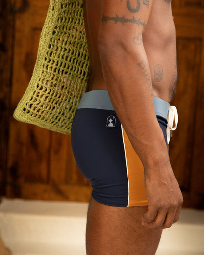 A man in a Dandy Del Mar Cassis Square Cut Swim Brief - Anchor holding a bag.