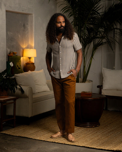 A man in a Dandy Del Mar Palma Shirt - Cacao Stripe standing in a living room.