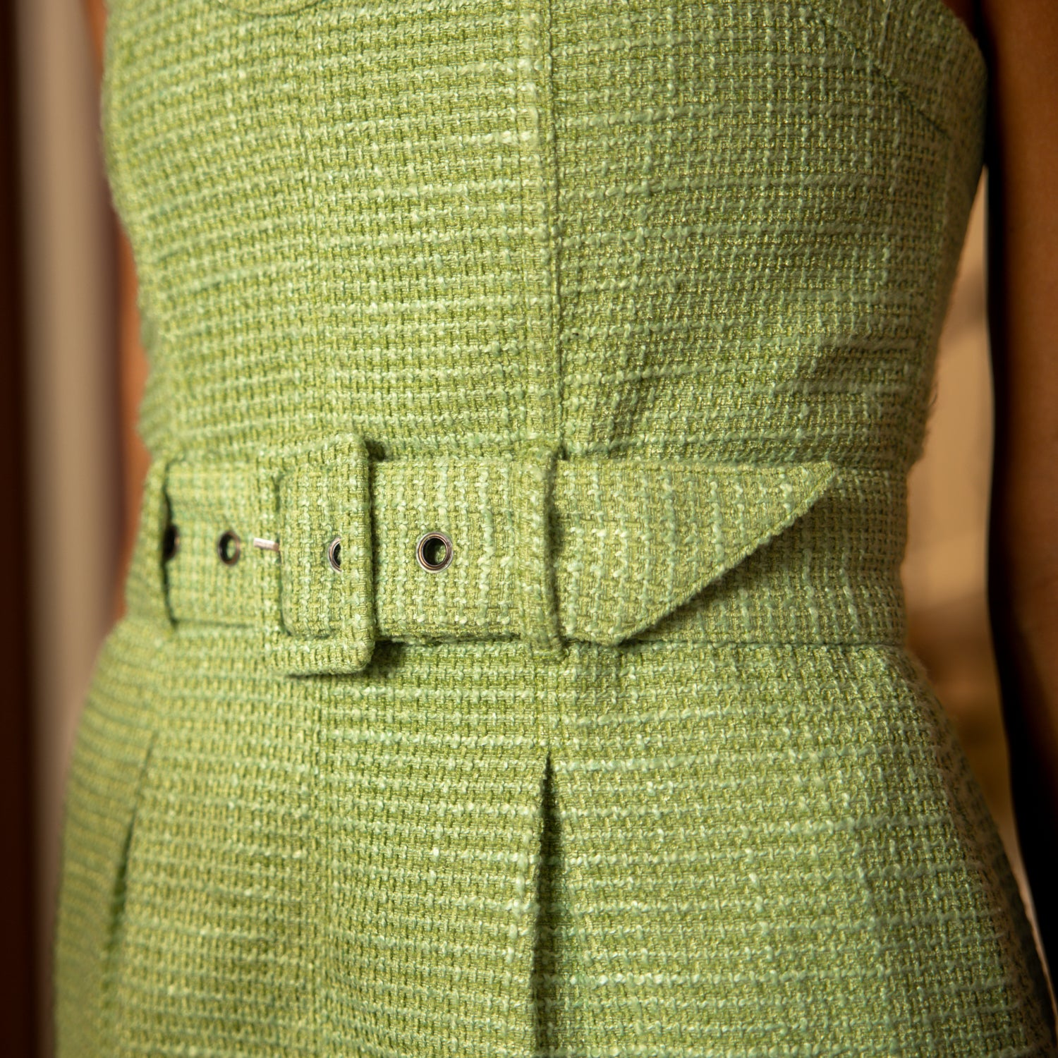 Close-up of a person in The Trinidad Tweed Strapless Dress - Oliva by Dandy Del Mar, featuring a wide belt and pleated details. The texture and stitching of the fabric are visible, highlighting the luxurious craftsmanship.