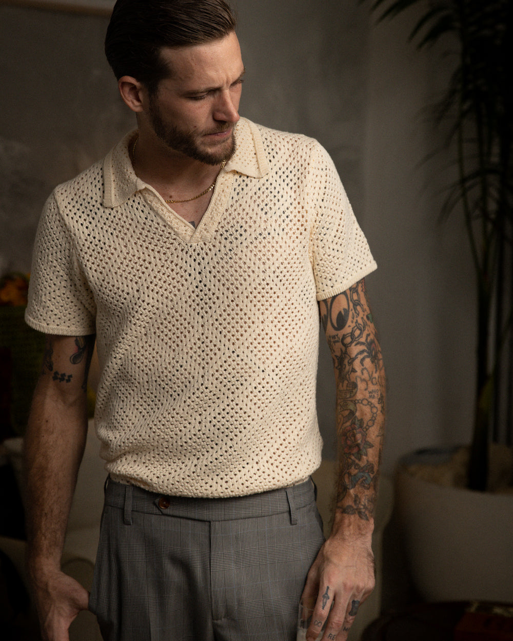 A man with tattoos standing in a living room, wearing The Antibes Crochet Shirt by Dandy Del Mar in Vintage Ivory.