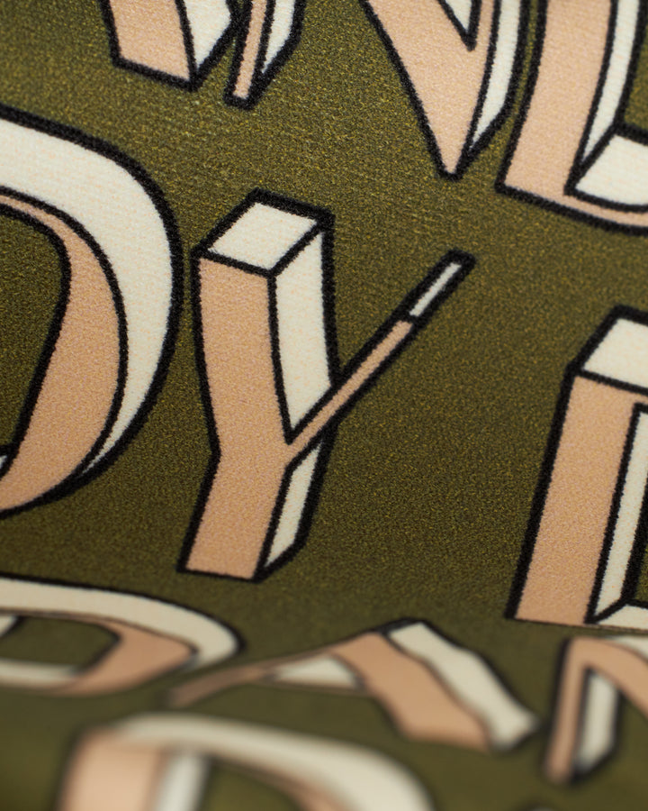 Close-up image of stylized, three-dimensional letters in beige and black on a textured green background, embodying Summer Leisure Chic vibes while highlighting The Hierro Top - Arbequina from Dandy Del Mar.