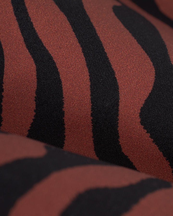 Close-up of fabric featuring a black and reddish-brown zebra stripe pattern, perfect for The Gomera Top - Onyx strapless swimwear crafted from recycled nylon by Dandy Del Mar.