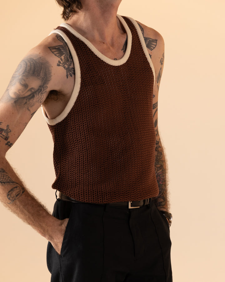 Someone wearing The Dominica Crochet Tank - Cappuccino by Dandy Del Mar and black pants shows off arm tattoos against a beige backdrop.