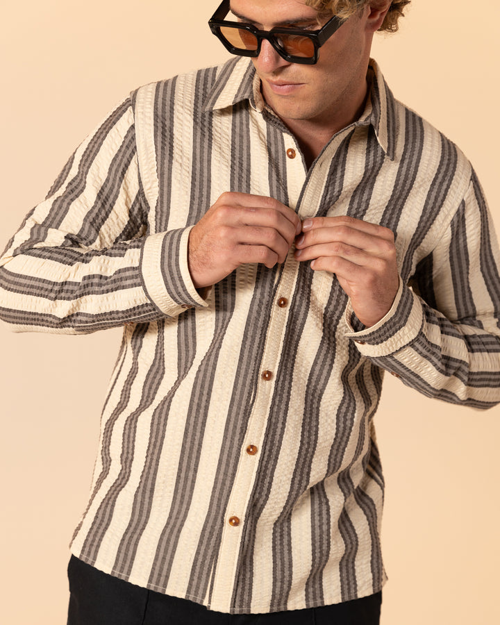 A person wearing sunglasses adjusts their Dandy Del Mar Santos Shirt in Tierra Weave against a neutral background.