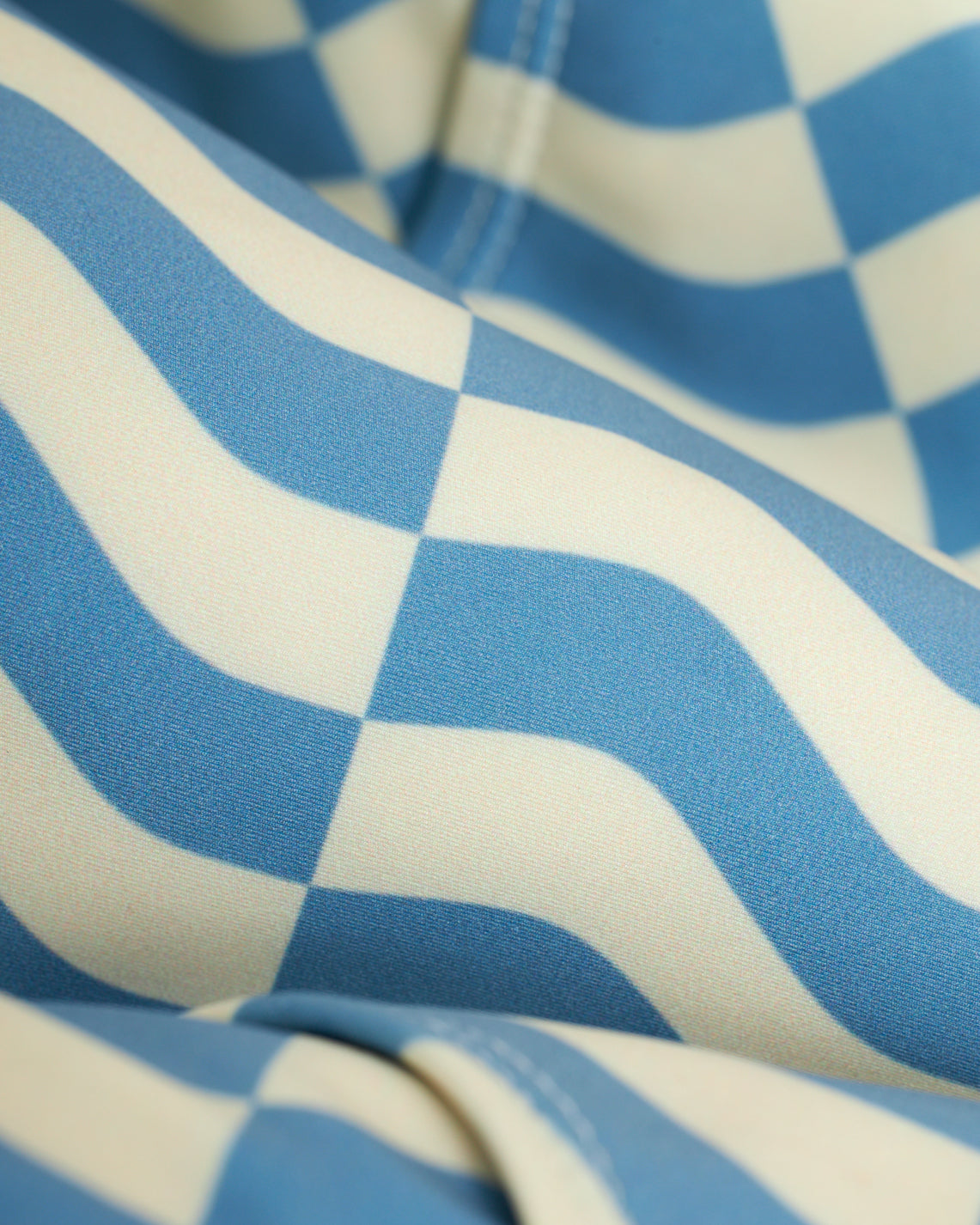 Close-up of fabric with a blue and white wavy checkered pattern, similar to Dandy Del Mar's The Belize Swim Briefs - Annapolis, crafted from recycled polyester for eco-friendliness.