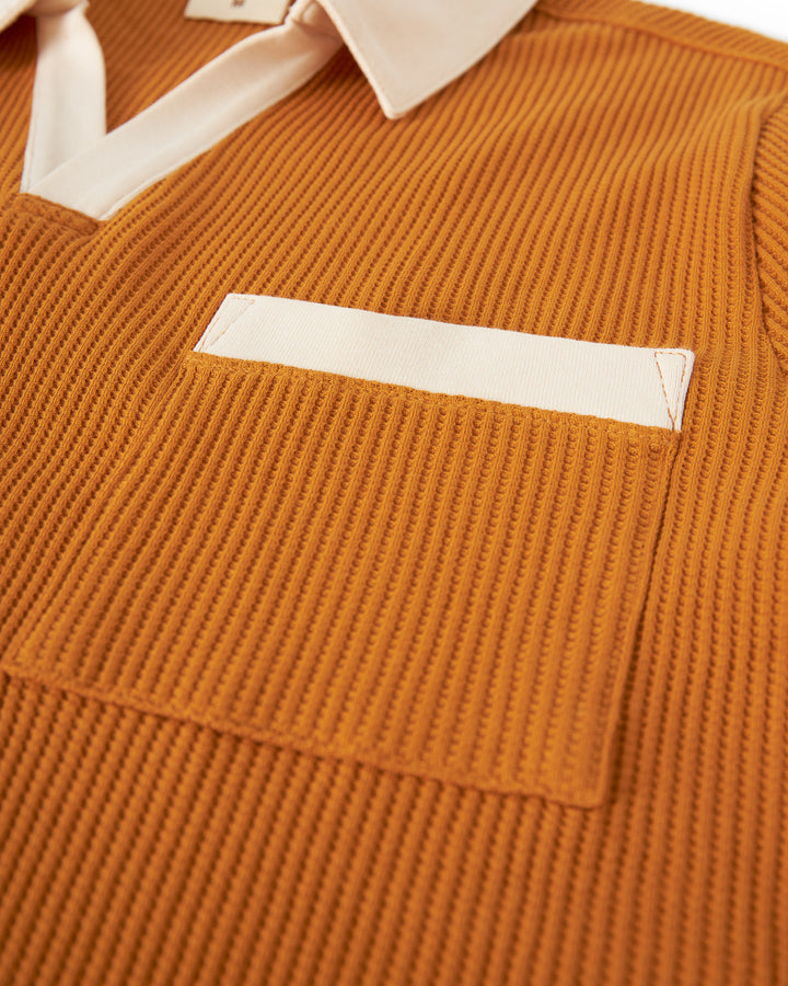 Close-up of an orange waffle knit The Cannes Waffle Knit Shirt - Burnt Sienna by Dandy Del Mar featuring a beige polo collar and a white chest pocket.