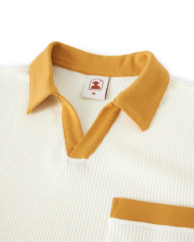 A close-up of The Cannes Waffle Knit Polo Shirt - Vintage Ivory by Dandy Del Mar, featuring a mustard yellow collar and chest pocket, soft waffle knit fabric, and a v-neck opening for a modern buttonless polo vibe.