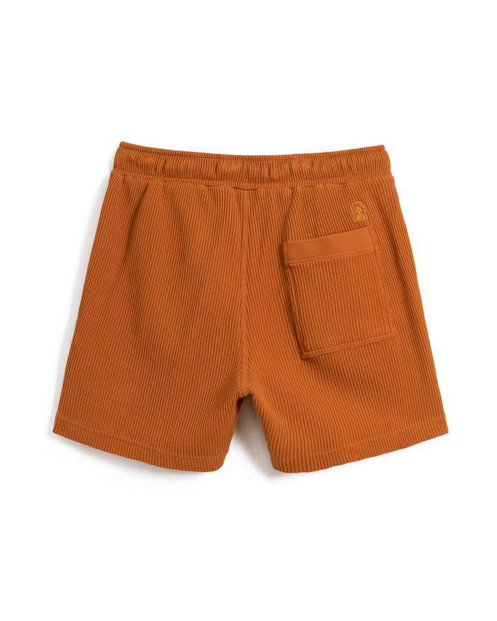 A pair of orange ribbed shorts with an elastic waistband, crafted from 100% cotton waffle knit fabric, featuring a convenient back pocket is now replaced by The Cannes Waffle Knit Shorts - Burnt Sienna from Dandy Del Mar.