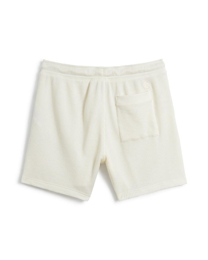 Rear view of a pair of off-white textured shorts, The Cannes Waffle Knit Shorts - Vintage Ivory by Dandy Del Mar, designed in waffle knit fabric, featuring an elastic waistband with a drawstring fit and a single small pocket on the left side.
