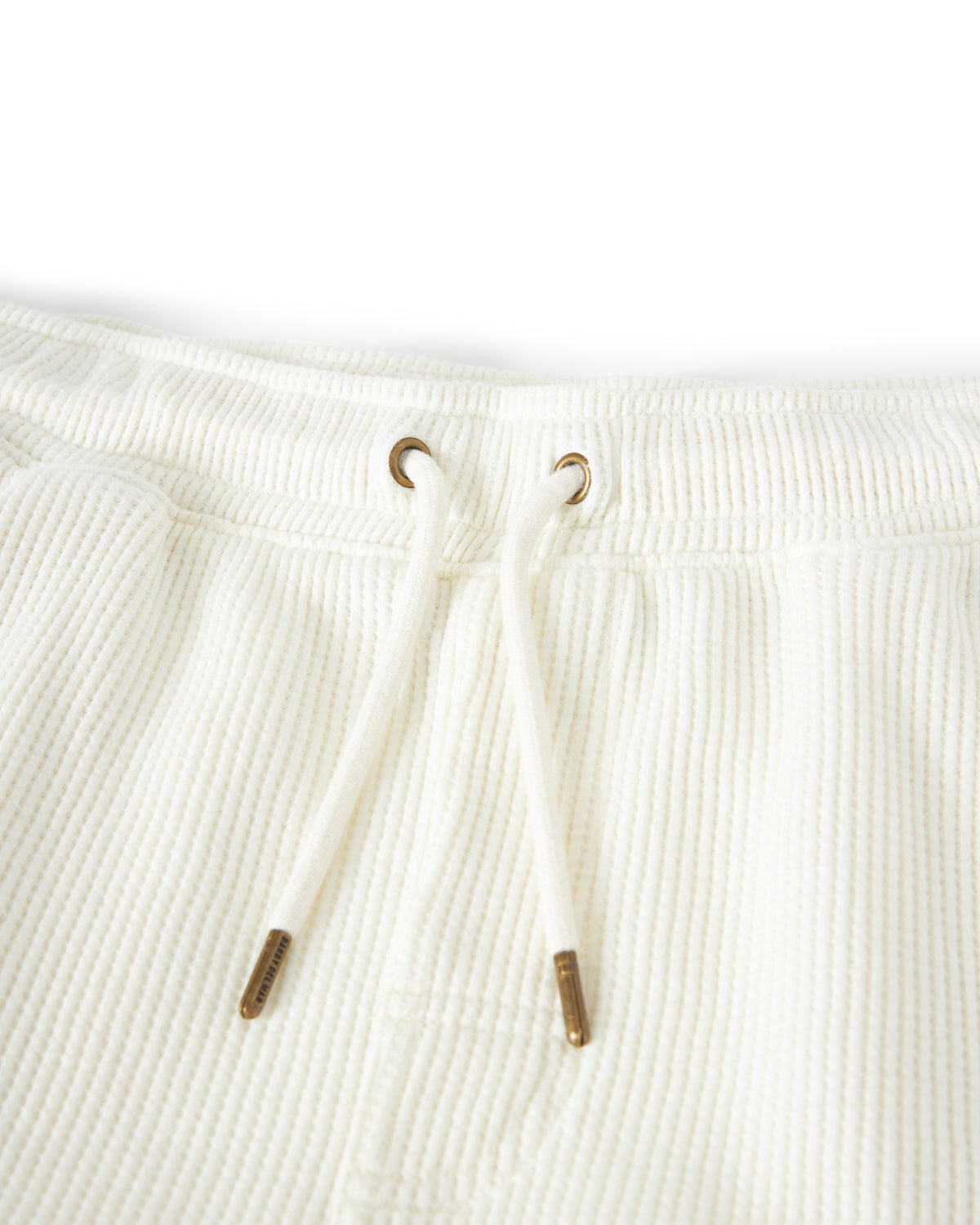 Close-up of the waistband of The Cannes Waffle Knit Shorts - Vintage Ivory by Dandy Del Mar, showing two metal grommets with a drawstring threaded through them.