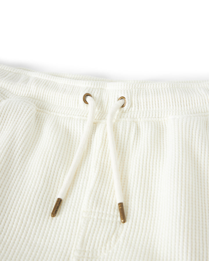 Close-up of the waistband of The Cannes Waffle Knit Shorts - Vintage Ivory by Dandy Del Mar, showing two metal grommets with a drawstring threaded through them.