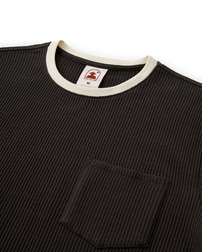 The Cannes Waffle Knit Tee - Albatross by Dandy Del Mar is a stylish black textured shirt with a waffle knit, featuring a round white-edged neckline, chest pocket, and an inner collar label with tree logo and size "M" for breathability.