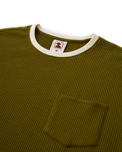 The Cannes Waffle Knit Tee - Arbequina by Dandy Del Mar is an olive green ribbed shirt featuring a contrast white collar lining, chest pocket, and a size M label in red and white on the collar.