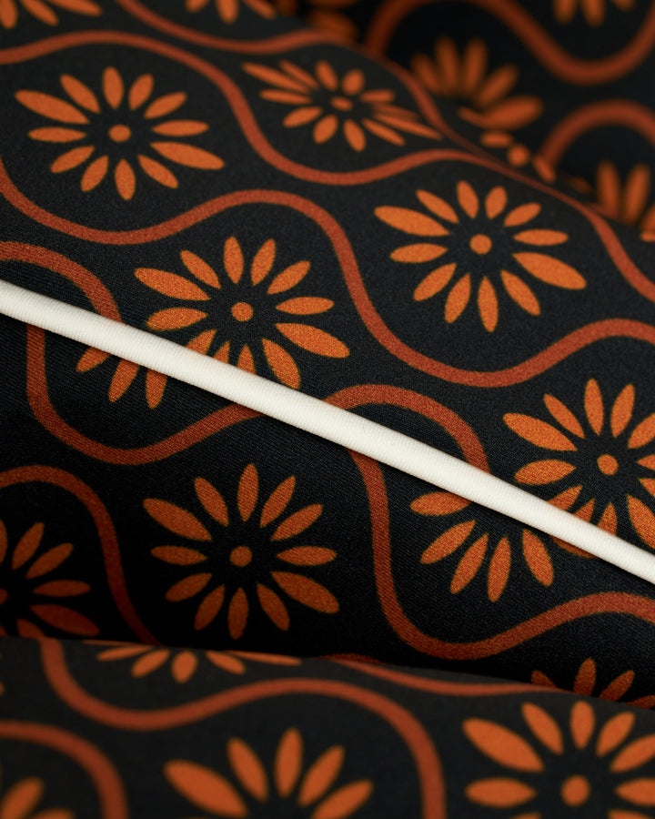 A close up of the Dandy Del Mar Cassis Square Cut Swim Brief - Cacao in orange and black fabric.