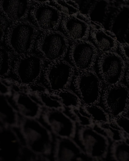 Close-up of a black, textured, open-knit fabric with a repeating pattern of oval-shaped holes, perfect for The Montserrat Crochet Skirt - Onyx by Dandy Del Mar.