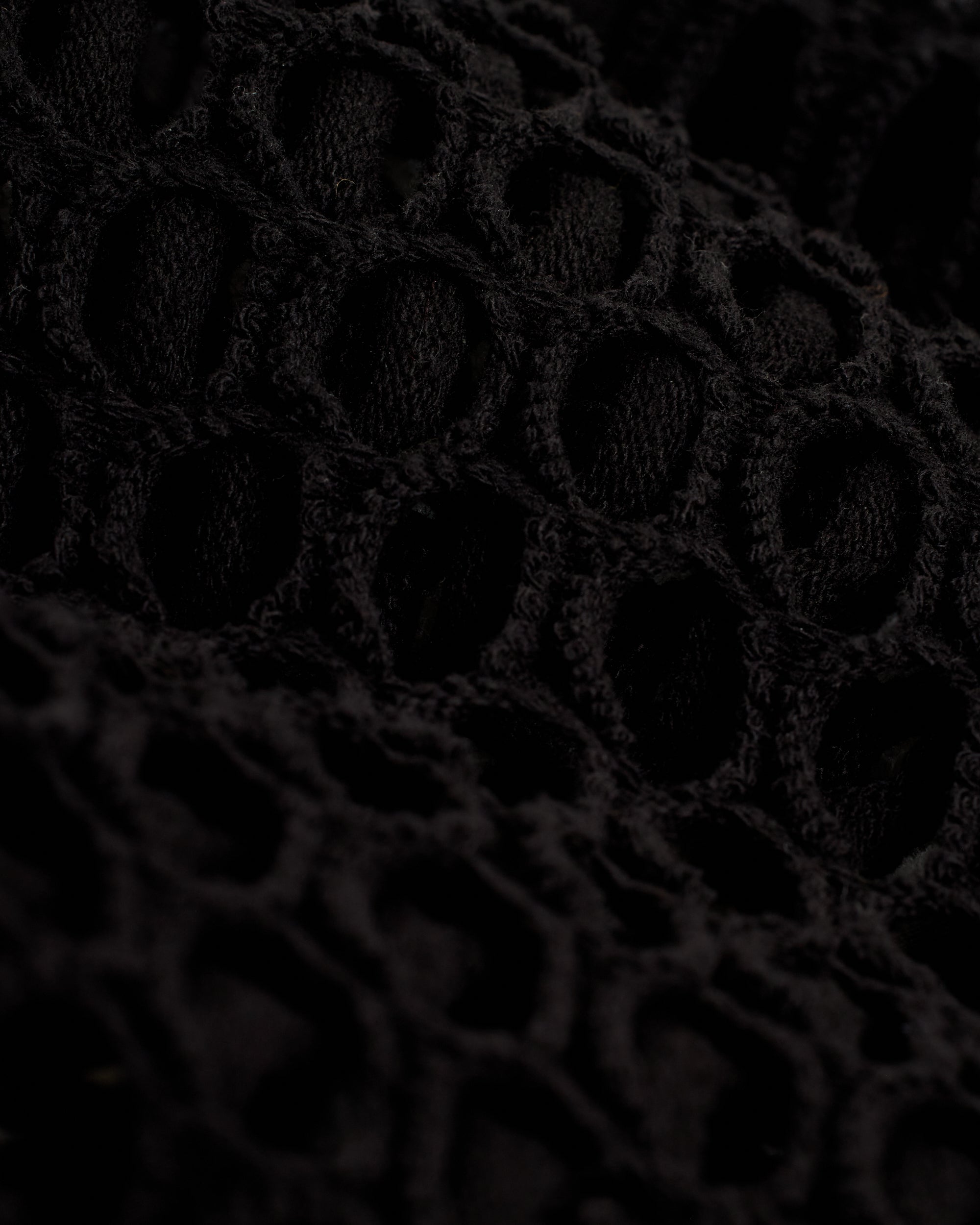 Close-up of The Montserrat Crochet Tank - Onyx by Dandy Del Mar, showcasing its black textured fabric with a honeycomb-like pattern of interlocking loops, reminiscent of diamond pattern crochet, creating an open, airy design.