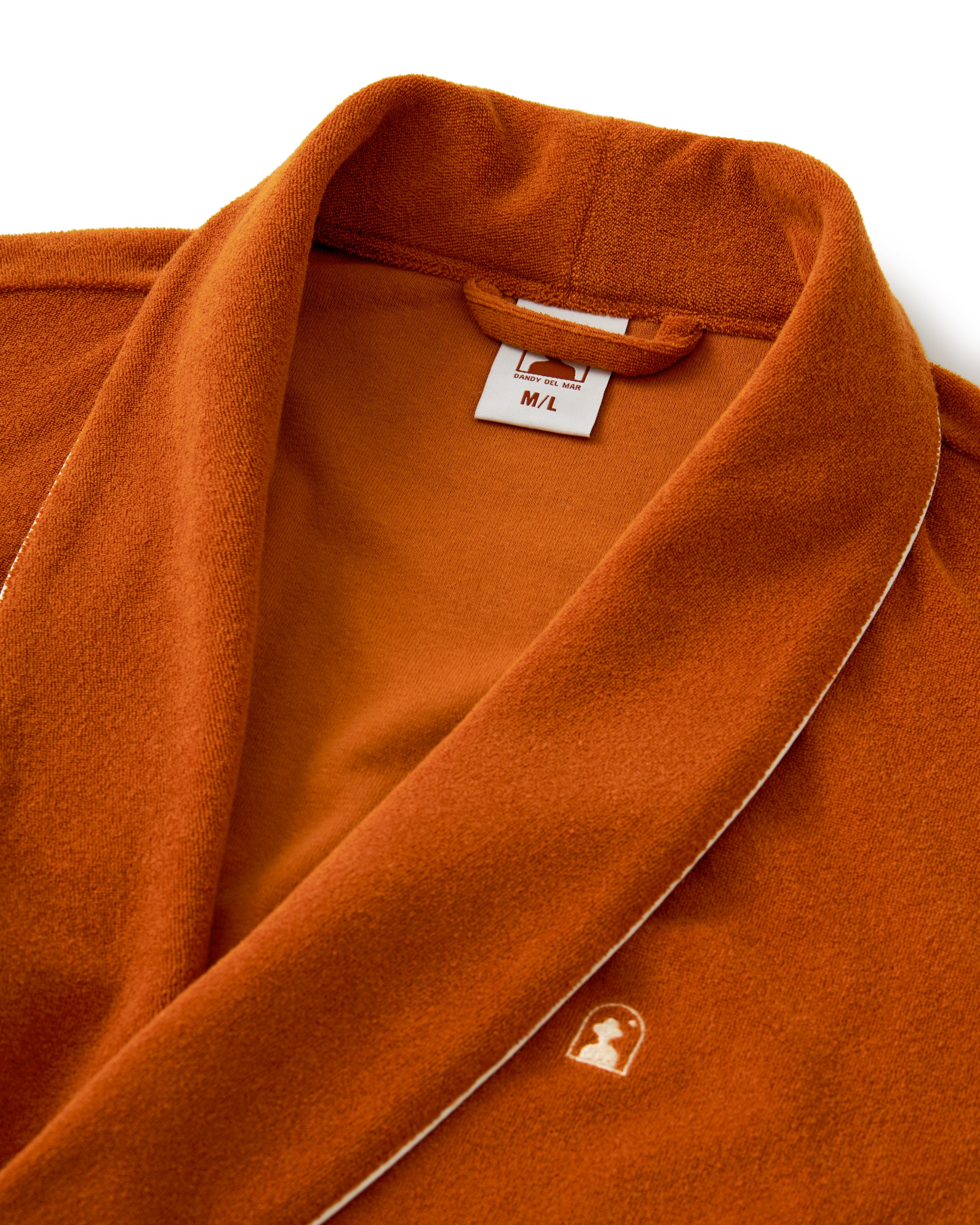 The Tropez Robe in Burnt Sienna by Dandy Del Mar is a medium/large ultra-soft Terry Cloth robe with an above-the-knee fit, features white trim and an embroidered hooded figure logo.