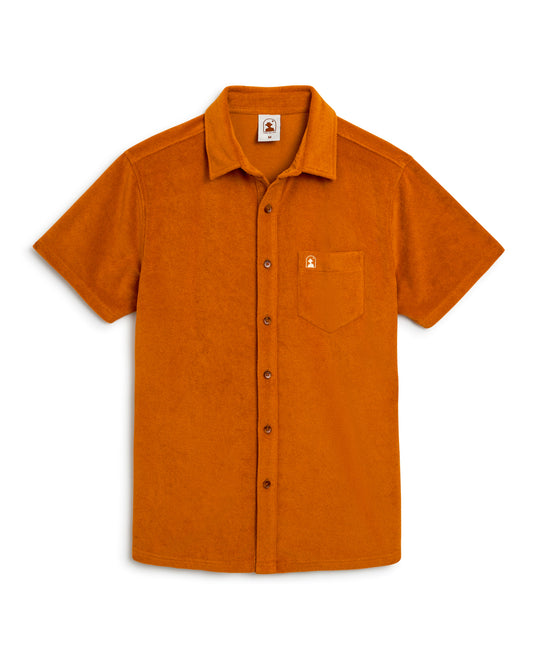 A short-sleeved, button-down shirt called The Tropez Terry Cloth Shirt - Burnt Sienna by Dandy Del Mar, featuring a small chest pocket with a branded patch above it and made from premium terry cloth.