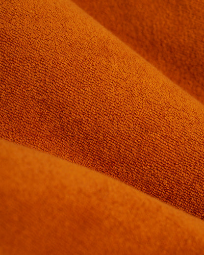 A close-up of burnt sienna terry cloth fabric from Dandy Del Mar's Tropez Shirt reveals soft, densely woven folds running diagonally, ideal for the Côte d'Azur.