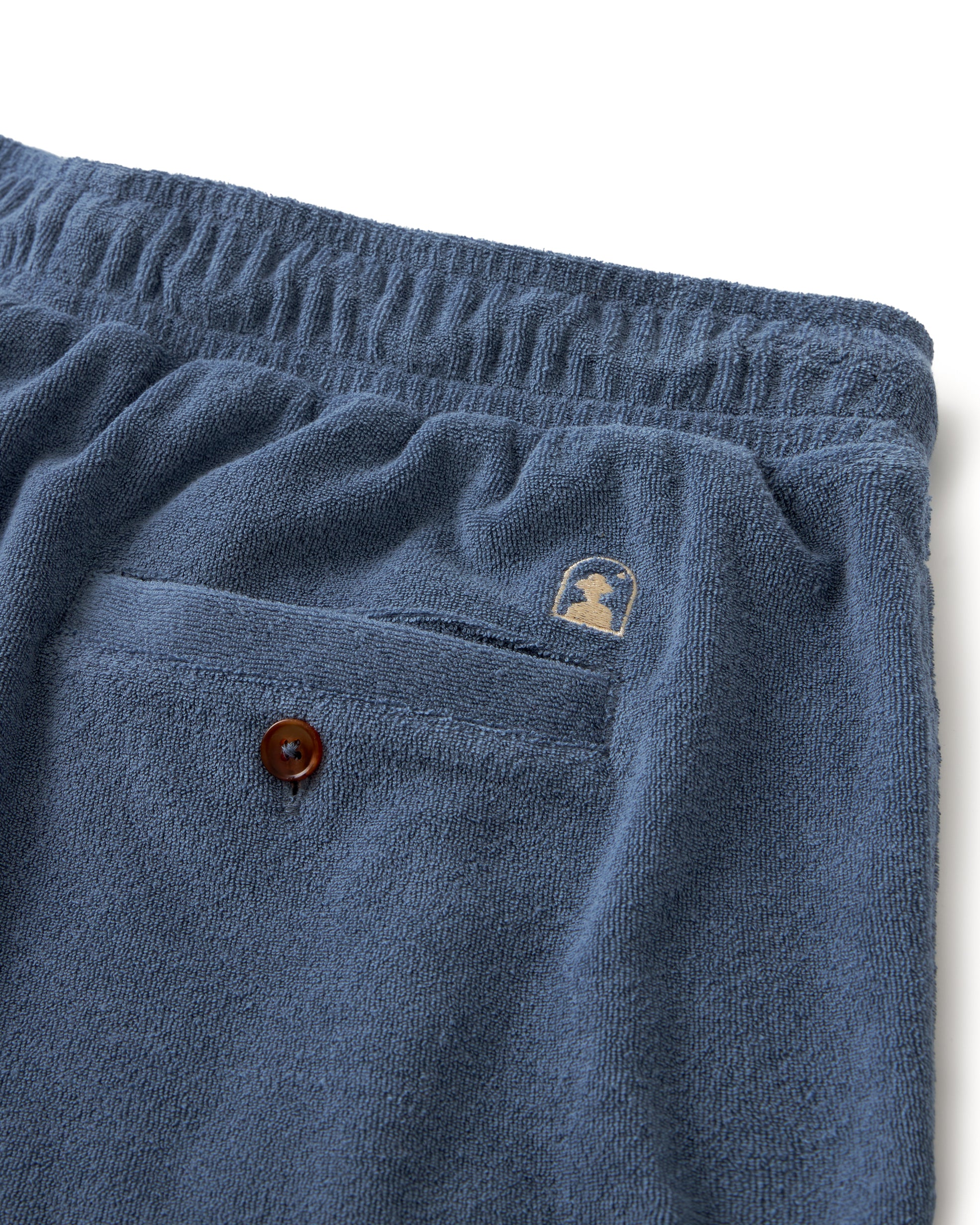 Close-up of The Tropez Short - Annapolis by Dandy Del Mar: Dark blue lounge shorts made from premium terry cloth with an elastic waistband and a small logo above a button-closure back pocket.