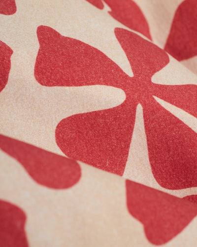 Close-up of beige fabric with a red abstract floral pattern, featured on The Ventura Volley Shorts - Currant by Dandy Del Mar—ideal for men's swimwear that stands out.