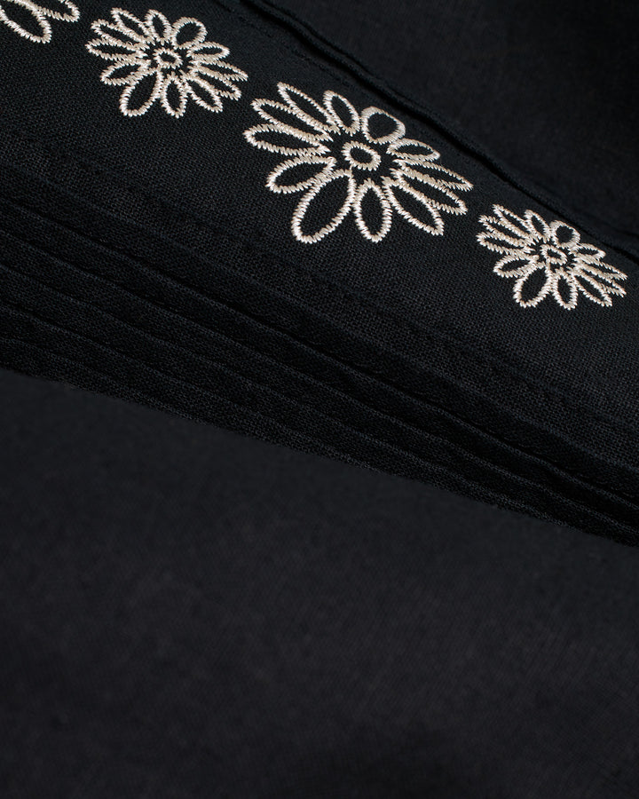 A close-up of a soft black Brisa Linen Shirt - Onyx by Dandy Del Mar with embroidered white flowers.